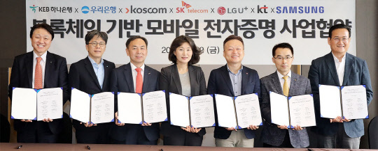 KEB하나은행, 우리은행, 코스콤으로 구성된 금융사들과 SK텔레콤, LG유플러스, KT로 구성된 통신 3사와 삼성전자는 사업협약식을 갖고 블록체인 기반의 모바일 전자증명 사업을 출범하기로 했다. 지난 12일 서울 중구 플라자호텔에서 개최된 협약식에서 7개 참여사 관계자들이 협약서를 들고 기념촬영을 하고 있다.   왼쪽부터 한준성 KEB하나은행 미래금융그룹 부행장, 황원철 우리은행 디지털금융그룹장 상무, 김계영 코스콤 미래성장본부장, 오세현 SK텔레콤 블록체인/인증 Unit장(전무), 이상민 LG유플러스 FC부문장(전무), 서영일 KT 블록체인비즈센터장(상무), 김주완 삼성전자 서비스기획그룹장(상무).  KEB하나은행 제공